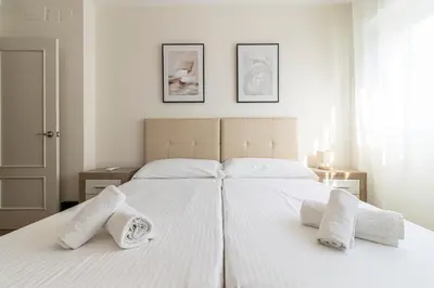 a white bedroom with two beds with towels on them at Allo Apartments Medina Duplex Parking 3 Habitaciones in Jerez de la Frontera