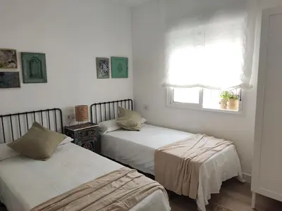 two beds in a white room with a window at Casa Bakio in Sanlúcar de Barrameda