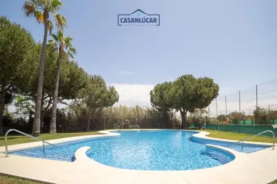 a swimming pool in a park with palm trees at Apartamento los jardines in Sanlúcar de Barrameda