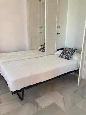 two beds in a room with white walls at ÁTICO Jardines de la salinera de VALDELAGRANA in El Puerto de Santa María