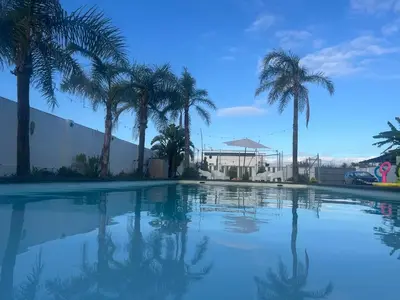 a swimming pool with palm trees and a building at Finca Rural Marmito in Sanlúcar de Barrameda