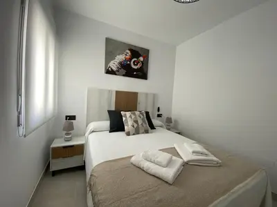 a white bedroom with a bed and a small table at Playa La Barrosa, AlojamientosLola in Chiclana de la Frontera