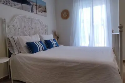 a bedroom with a white bed with blue pillows and a window at Precioso apartamento en Rota in Rota
