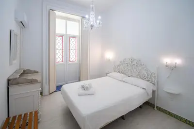 a white bedroom with a white bed and a chandelier at Montera Suite Cádiz in Cádiz