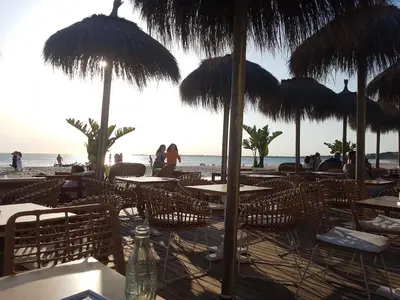 a restaurant with tables and straw umbrellas on the beach at Vistahermosa-El ancla in El Puerto de Santa María