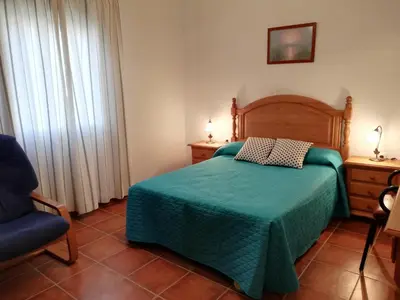 a bedroom with a bed with a green blanket and a chair at Chalet Casa Paqui solo familias o parejas in Conil de la Frontera