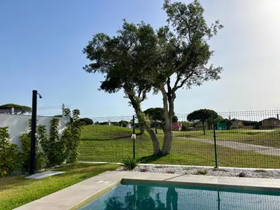 a swimming pool in front of a fence with a tree at Poniente Beach House in Chiclana de la Frontera