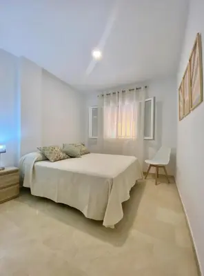a white bedroom with a bed and a chair at Novo Sancti Petri LUZ DEL NOVO in Novo Sancti Petri