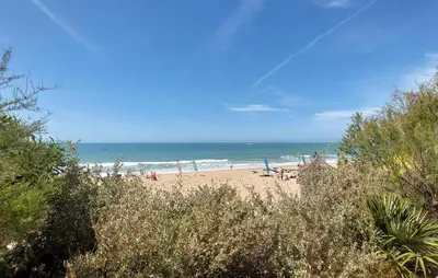 a beach with people sitting on the sand and the ocean at Nice Home In Chiclana De La Fronter in Novo Sancti Petri