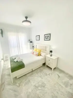 a white bedroom with a bed and a night stand at Apartamento Atlántico in Rota