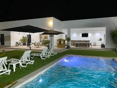a swimming pool with white chairs and an umbrella at Villa con piscina Camino Doñana in Sanlúcar de Barrameda