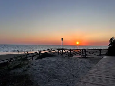 a sunset at the beach with a wooden boardwalk at Luxury Beach Townhouse Retreat in Cádiz