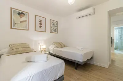 two beds in a room with white walls and wood floors at Allo Apartments Morenos III Bajo A Centro 2 Habitaciones in Jerez de la Frontera