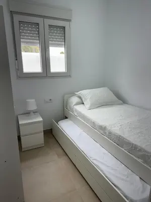 a white bedroom with a bed and two windows at Apartamento El Oasis in Chiclana de la Frontera
