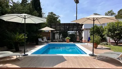 a swimming pool with two umbrellas and two chairs at Abajo Stijlvol appartement met zwembad en tuin in Cádiz