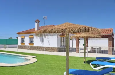 a large straw umbrella with chairs and a swimming pool at Alojamiento Rural Las Quintas in Conil de la Frontera