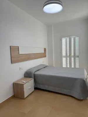a white bedroom with a bed and a light at Piso Centro Chiclana in Chiclana de la Frontera