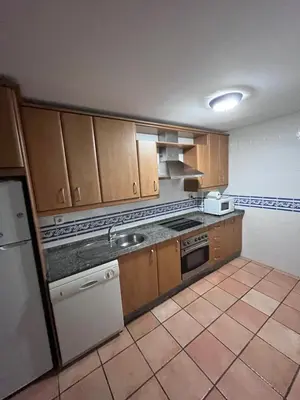 a kitchen with wooden cabinets and a white appliance at Adosado con jardín Urb Galia Ballena in Cádiz