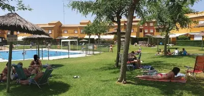 a group of people sitting in lawn chairs by a pool at Adosado con jardín Urb Galia Ballena in Cádiz