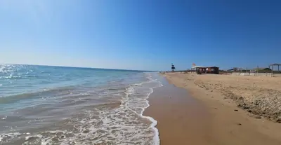a sandy beach with the ocean on a clear day at Chipiona - Playa a 200m terraza piscina padel in Chipiona