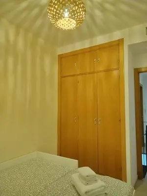 a bedroom with a bed and wooden cabinets and a chandelier at Dúplex Chiclana Centro con Terraza y Parking By Chiclana Dreams in Chiclana de la Frontera