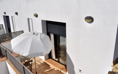 a white house with an umbrella and a balcony at Apartamento en Casa Palacio- Centro Sanlucar in Sanlúcar de Barrameda