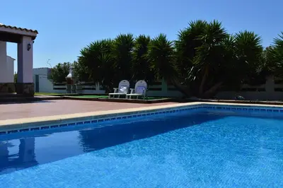 a swimming pool with two chairs and palm trees at Las Yucas in Conil de la Frontera
