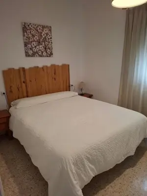 a bedroom with a white bed with a wooden headboard at Apartamento Las Arenas in Chiclana de la Frontera