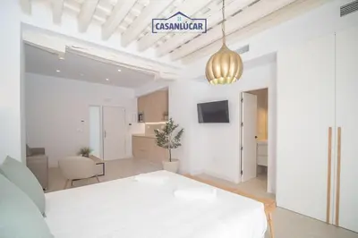 a white room with a white bed and a kitchen at Sanlucar Centro - Apartamento 1 in Sanlúcar de Barrameda