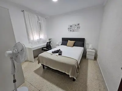 a white bedroom with a bed and a fan at Apartamento Granja - a 5 min de la playa in Cádiz