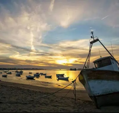 a group of boats sitting on the beach at sunset at Apartamento V CENTENARIO BEACH Sanlúcar in Sanlúcar de Barrameda