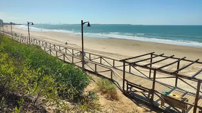 a wooden staircase leading to a beach with the ocean at Pantoque Sani Ideal para familias in El Puerto de Santa María