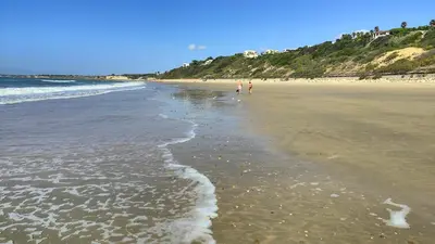 a beach with two people walking on the sand at Pantoque Sani Ideal para familias in El Puerto de Santa María