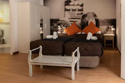 a bedroom with a bed with orange pillows and a chair at Hotel Alquimia Cadiz in Cádiz