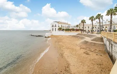 a beach with a building and palm trees and the ocean at 2 Bedroom Amazing Apartment In Chipiona in Chipiona