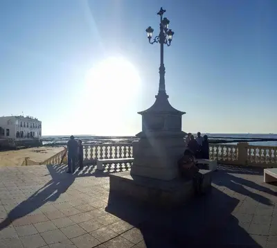 a person sitting on a bench next to a statue at las olas in Chipiona