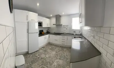 a white kitchen with white cabinets and a tile floor at Adosado Casa Melo Playa la Barrosa La Balconera in Poblado de Sancti Petri