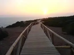 a wooden boardwalk on the beach with the sun in the background at VillaConil in Conil de la Frontera