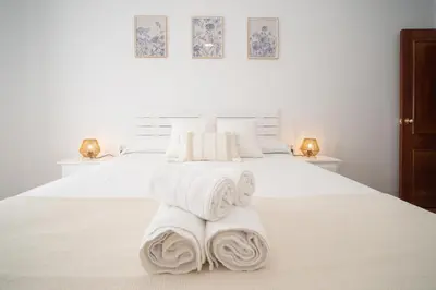 a white bedroom with two beds with towels on them at SibsSanlucar Azahar Centrico Vistas Terraza Coqueto in Sanlúcar de Barrameda
