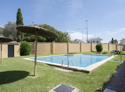 a swimming pool with an umbrella in the grass at Chalet Pareado & Piscina in El Puerto de Santa María