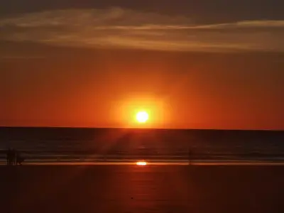 a sunset on the beach with people walking on the beach at Bonita casa cerca de la playa in Chipiona
