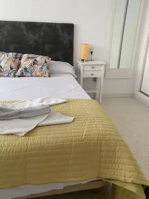 a bedroom with a bed with a yellow blanket and a table at Bonita casa cerca de la playa in Chipiona