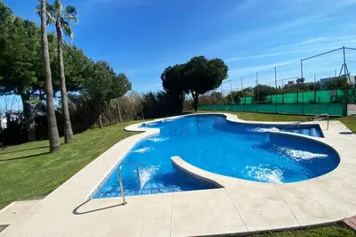 a large blue swimming pool with a tennis court at Apartamento Jara, playa, piscina, AC, Wi-Fi in Sanlúcar de Barrameda