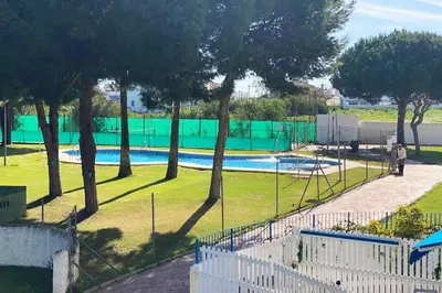 a person standing next to a swimming pool with trees at Apartamento Jara, playa, piscina, AC, Wi-Fi in Sanlúcar de Barrameda