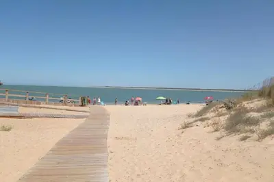 a boardwalk on a beach with people on the beach at Apartamento Jara, playa, piscina, AC, Wi-Fi in Sanlúcar de Barrameda