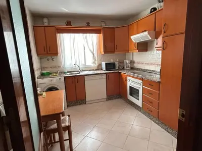 a small kitchen with wooden cabinets and a window at La Marina, apartamento in Sanlúcar de Barrameda