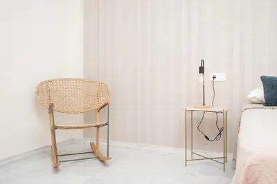 a rattan chair in a bedroom with a side table at Apartamento Centro Sanlucar - Banda Playa in Sanlúcar de Barrameda