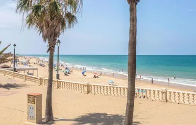 a beach with palm trees and people on the beach at Nice Apartment In Chipiona With Wifi in Chipiona
