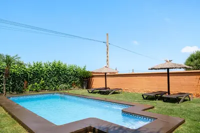 a swimming pool in a yard with two tables and umbrellas at Villa Marta Clara in Conil de la Frontera