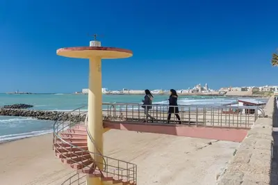 two people walking on a boardwalk next to the beach at Apartamento Miracadiz in Cádiz